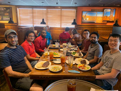 Large group pic of people around a table at a restaurant, 2 in red shirts